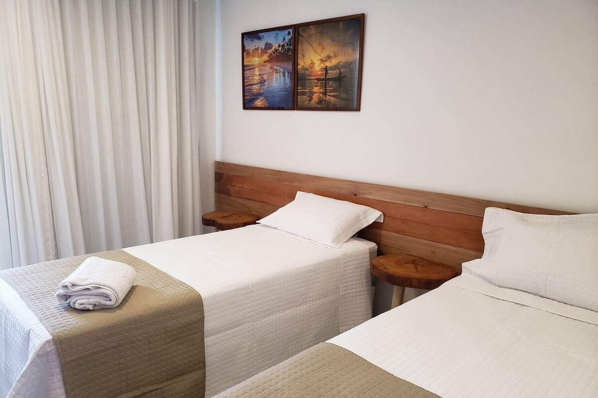 Une chambre d’hôtel avec deux lits, une tête de lit en bois, un tableau au mur et une fenêtre avec des rideaux.