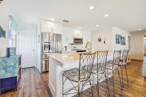 A modern kitchen with white cabinetry, stainless steel appliances, and a central island with bar stools.