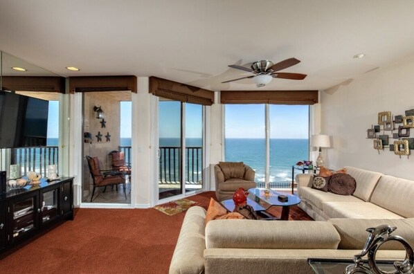 A spacious living room with a large window offering a view of the ocean, a ceiling fan, and a television on a cabinet. - BEAUTIFUL OCEAN VIEW--STEPS TO THE BEACH (Solana Beach)