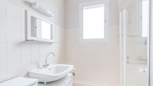 Ein modernes Badezimmer mit einem weißen Waschbecken, einem Spiegel und einer Dusche.