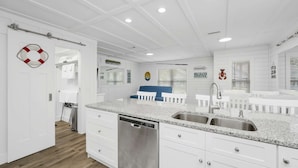 A modern kitchen with white cabinetry, granite countertops, a dishwasher, and a large sink. - Sunset Escapes B (Panama City Beach)