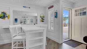 A white interior with a dining table and chairs, a kitchen area, and a door labeled "CLAW DIGGERS". - Sunset Escapes B (Panama City Beach)