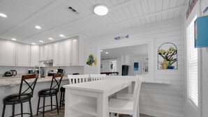 A modern kitchen with white cabinetry, a white dining table, and bar stools. - Sunset Escapes B (Panama City Beach)