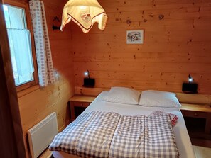 A wooden cabin room with a bed, two bedside tables, a window with curtains, and a wall-mounted picture. - Private apartment in a chalet at the base of the slopes, sleeps 5–7, south-facing terrace (Les Orres)