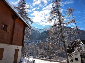 Ein Holzgebäude mit schneebedecktem Dach, einer Treppe und Blick auf verschneite Bäume und Berge.