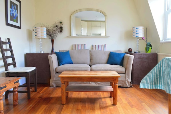 A living room with a sofa, a wooden table, a chair, a mirror, and a lamp.