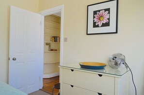 A room with a white door, a glass-top table with a bowl and fan, a bookshelf, and a framed flower on the wall.