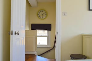 Un couloir avec une horloge, une fenêtre, un radiateur et une porte.