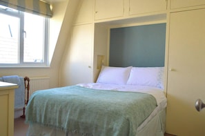 A bedroom with a bed, a window, a radiator, and a door.
