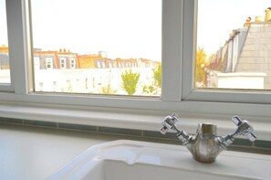 Una ventana con vista a casas escalonadas, un lavamanos blanco y un grifo.