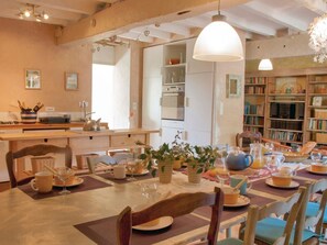 A dining area with a table set for a meal, surrounded by chairs, and a kitchen area with cabinets and appliances in the background.