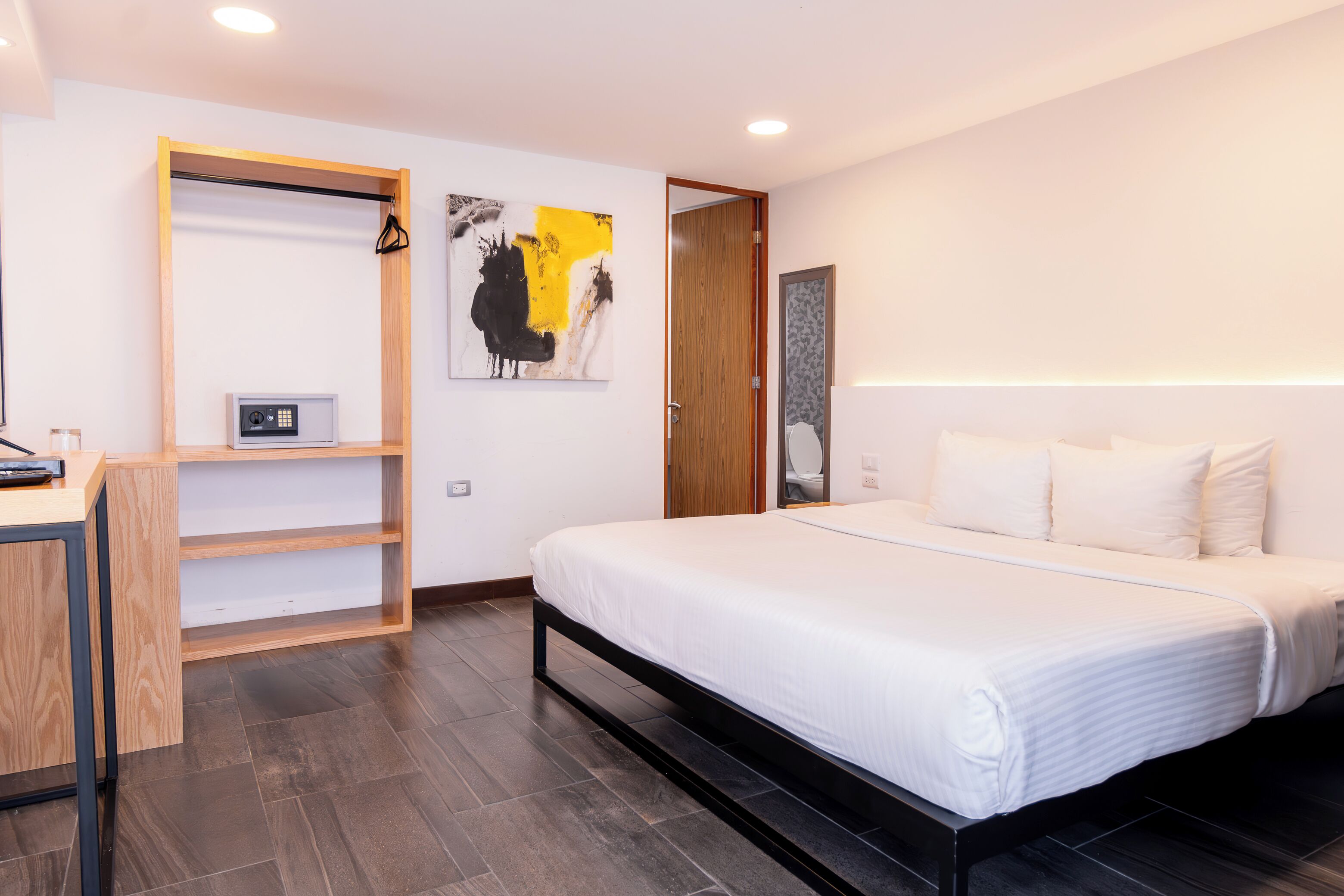 Un dormitorio moderno con cama, un escritorio de madera, una estantería y una puerta que da a otra habitación.