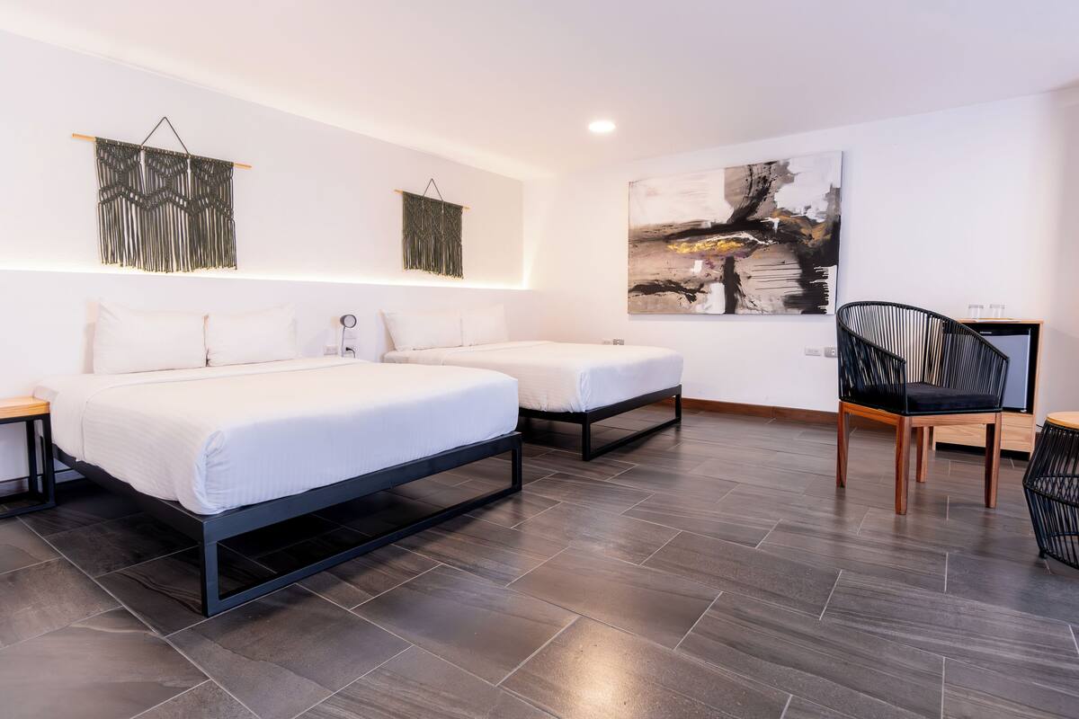 A modern hotel room with two beds, a black chair, and a painting on the wall.