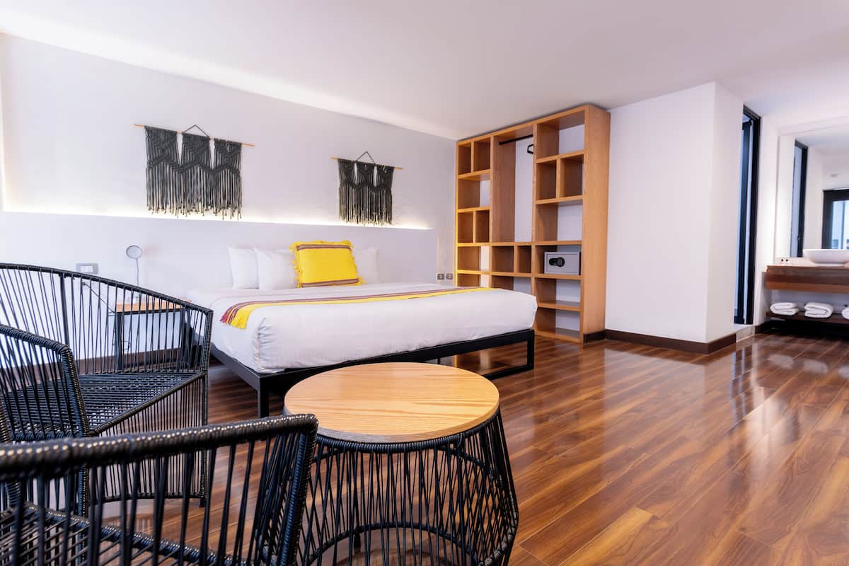 A modern hotel room with a bed, a wooden side table, a round chair, and a built-in bookshelf.