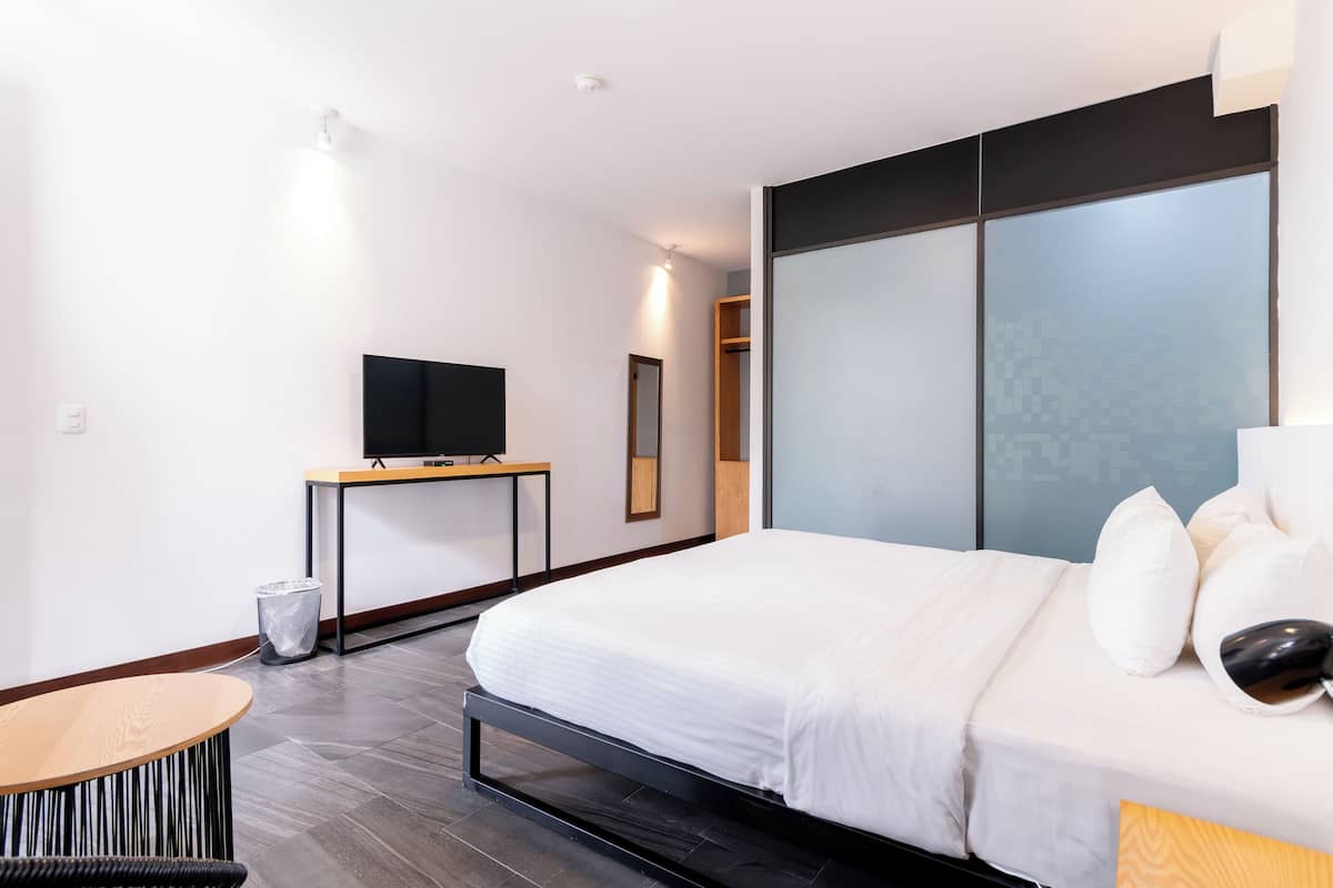 A modern hotel room with a bed, a TV on a small table, and a large window with a view.