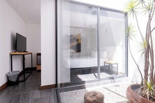 Een moderne kamer met een bed, een televisie op een standaard, een tafeltje en een potplant.