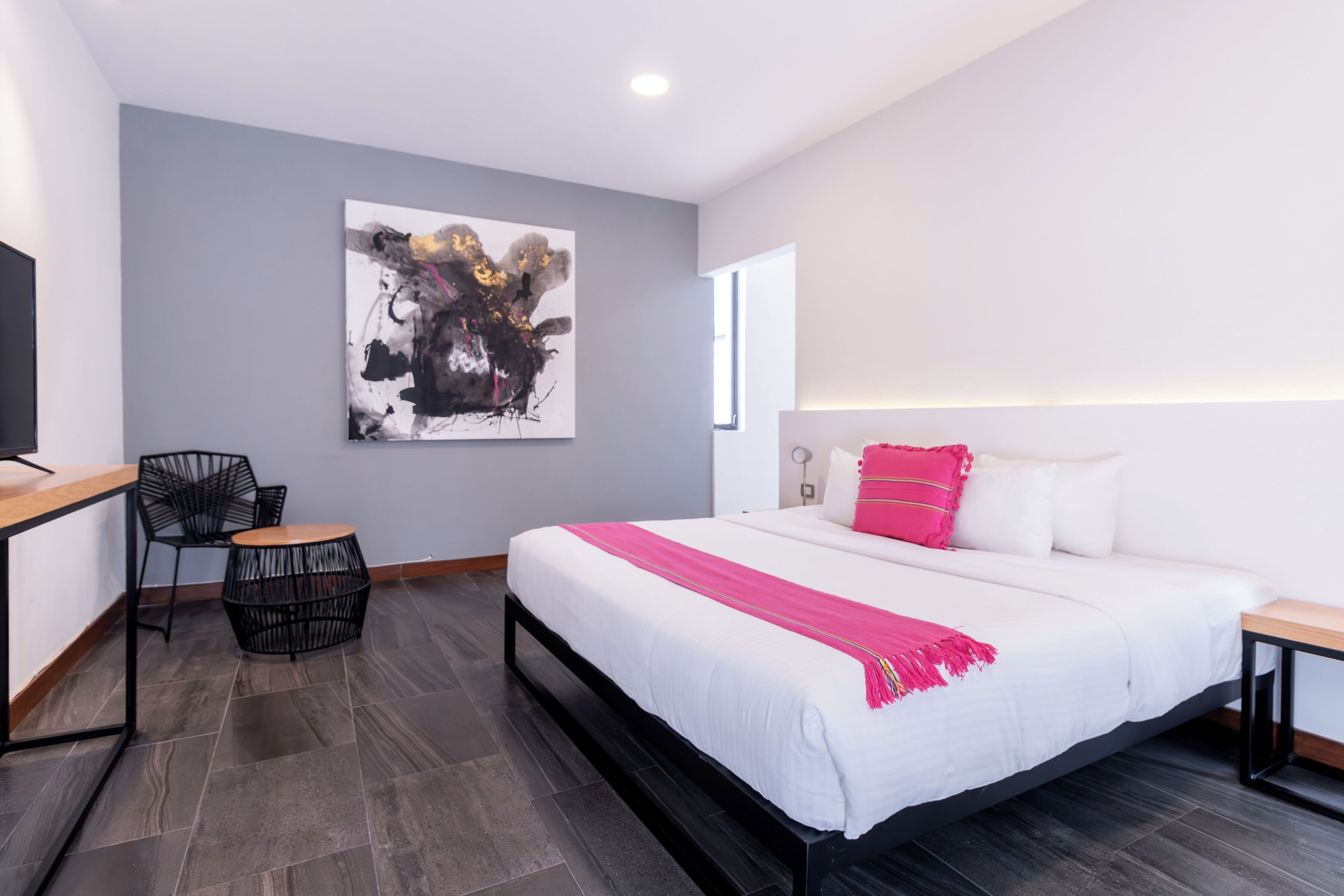 Une chambre d’hôtel moderne avec un grand lit, un bureau avec une chaise, une table ronde et un grand tableau abstrait accroché au mur.
