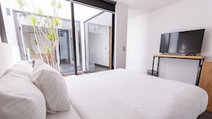 Ein modernes Hotelzimmer mit einem großen Bett, einem Flachbildfernseher auf einem Holzständer und einer Glasschiebetür zu einem Außenbereich.
