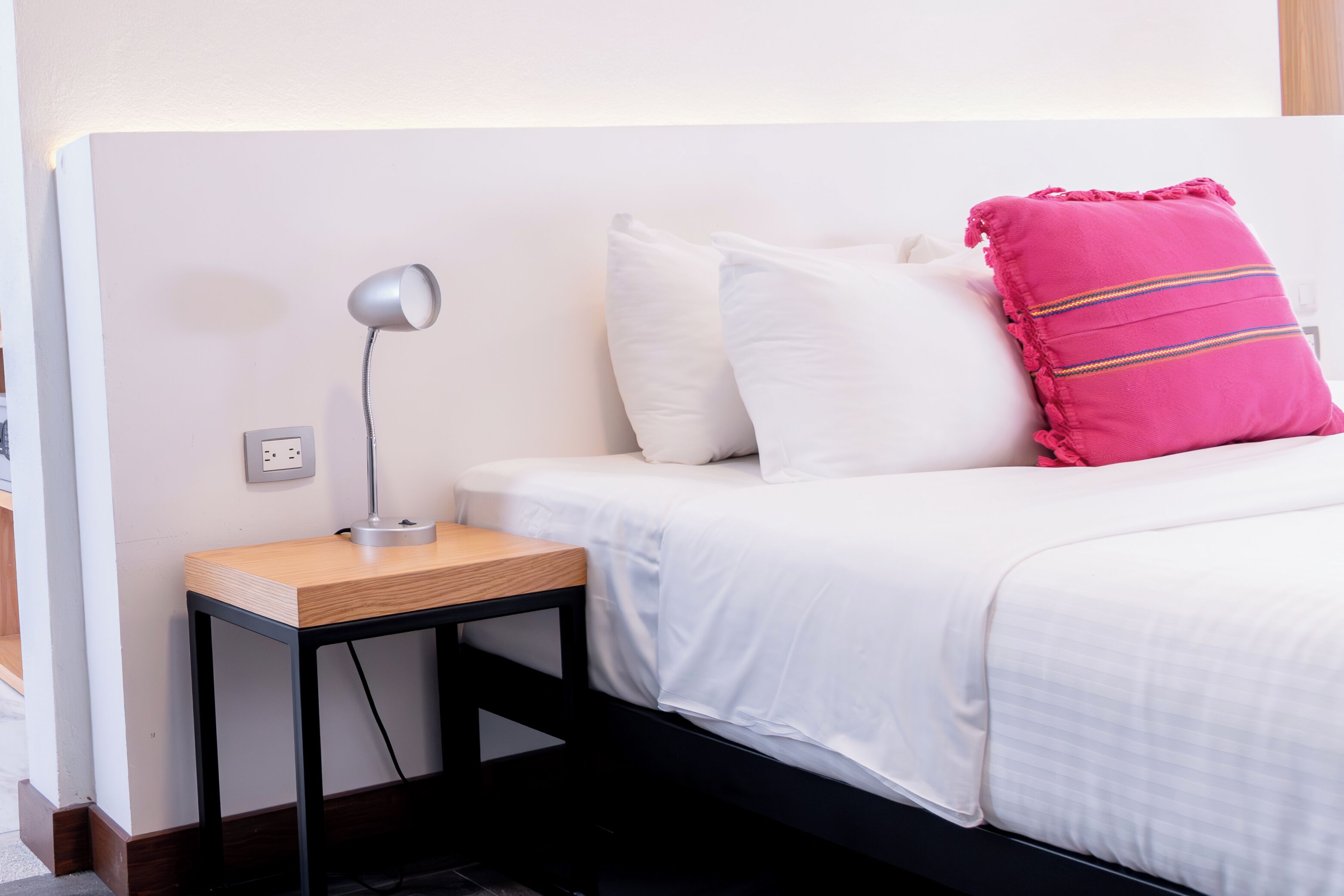 A neatly made bed with white bedding and a single pink pillow with stripes.