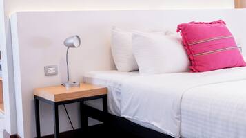 A neatly made bed with white bedding and a single pink pillow with stripes.
