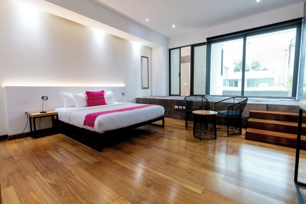 A modern hotel room with a large bed, a desk, and a chair, a staircase, and a large window with a view.