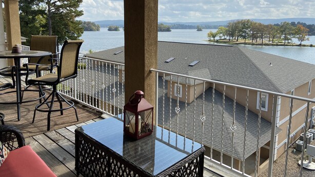 A balcony with a table, chairs, and a view of a lake and distant hills. - Relaxing Lake View Condo (Hot Springs)