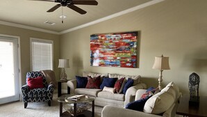 A living room with a beige sofa, patterned armchair, and a coffee table. There is a ceiling fan, a painting on the wall, and a lamp on a side table. - Relaxing Lake View Condo (Hot Springs)