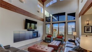 A spacious living room with a large TV, comfortable seating, and large windows offering a view of the mountains. - Amazing Mountain Home w/ 360 degree mountain views, hot tub and outdoor deck.   (Crested Butte)
