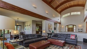 A spacious living room with a high ceiling, leather sofas, a patterned rug, and a dining area with a table and chairs. - Amazing Mountain Home w/ 360 degree mountain views, hot tub and outdoor deck.   (Crested Butte)