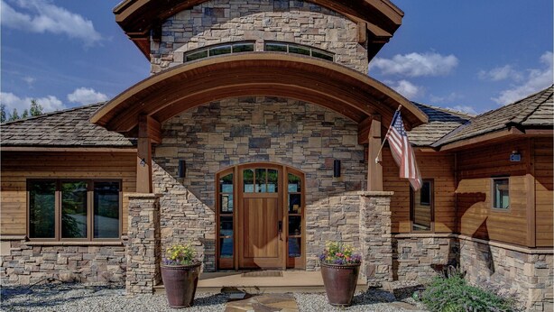 A stone and wood house with a large wooden arch over the entrance, a flag, and two potted plants. - Amazing Mountain Home w/ 360 degree mountain views, hot tub and outdoor deck.   (Crested Butte)