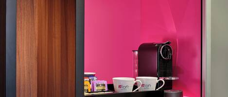A coffee machine, two white mugs, and a tea box on a black countertop.