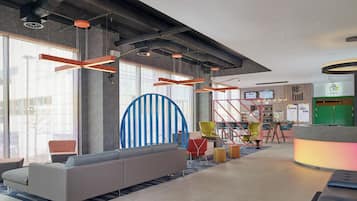 A modern lobby with a grey sofa, colorful chairs, a blue and white striped wall, and a reception desk with a green sign.