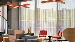 A modern living room with a sofa, ottomans, a red chair, and a glass coffee table. - Aloft by Marriott Birmingham Eastside (Birmingham)