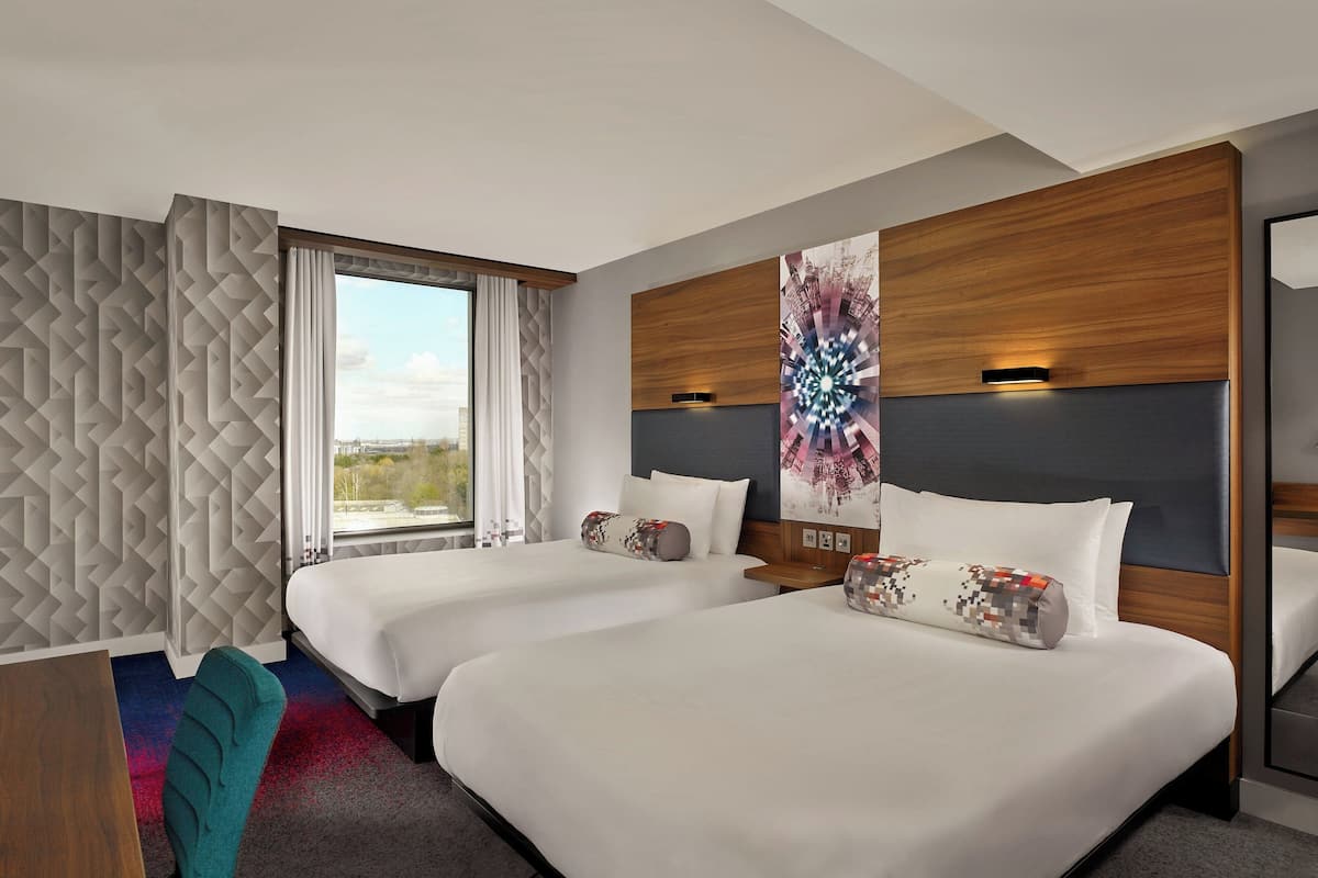 A hotel room with two beds, a large window, and a view of the outdoors.