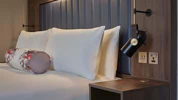 A neatly made bed with white linens and a patterned pillow, a bedside lamp, and a wooden nightstand with a drawer.