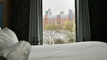 A hotel room with a bed, a window with curtains, and a view of a cityscape.