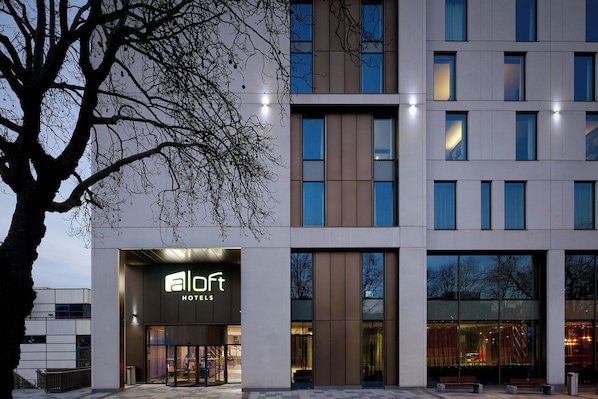 A modern hotel with a prominent 'aloft' sign, large windows, and a tree in the foreground.