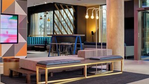 A modern lounge area with a bench, seating, and a TV screen. - Aloft by Marriott Birmingham Eastside (Birmingham)