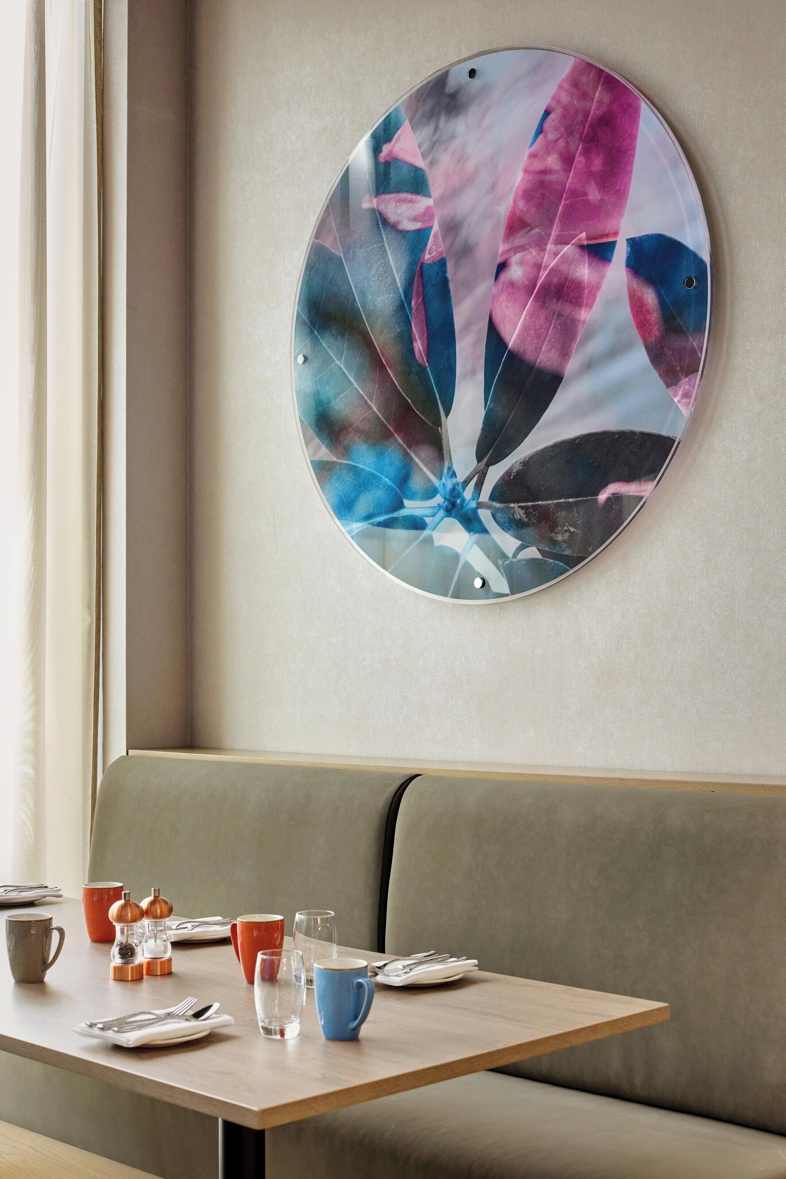 Un comedor con una obra de arte circular en la pared, una mesa preparada con platos, vasos y cubiertos, y un banco acolchado.