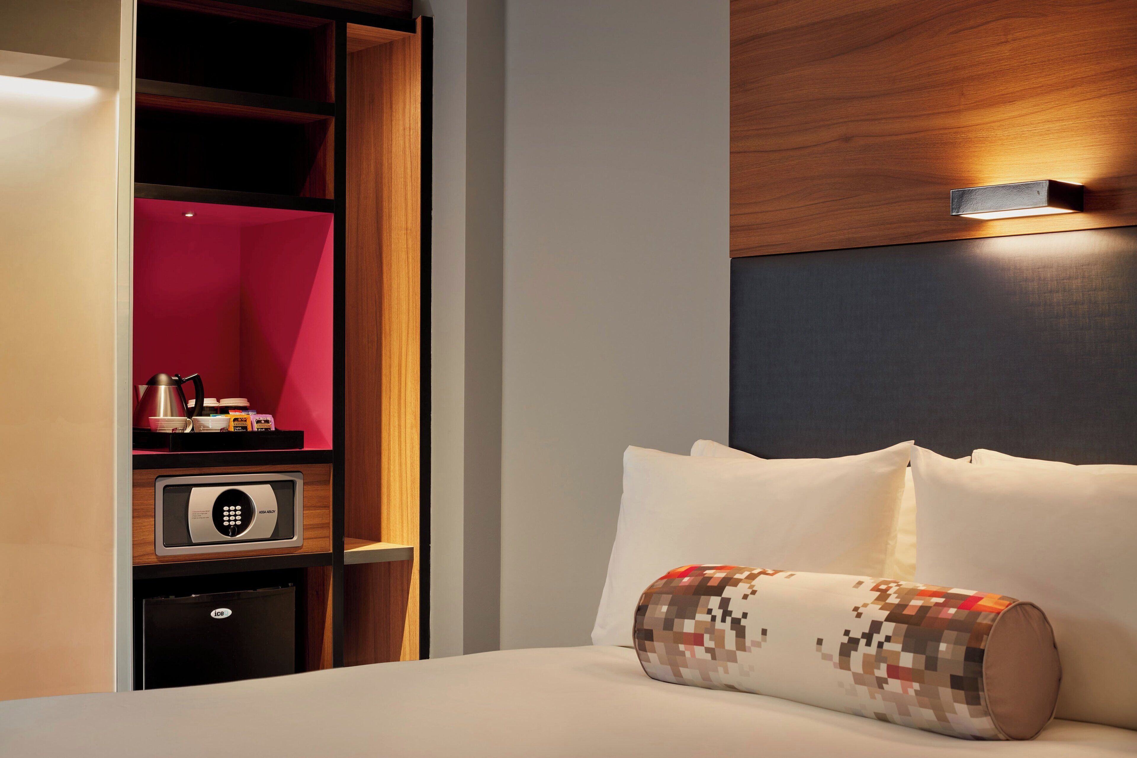A hotel room with a bed, a pillow, a digital safe, and a minibar.