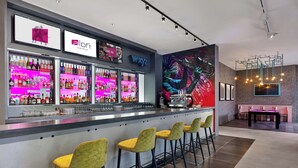 A bar area with a neon-lit liquor display, a large mural, and a seating area with a table and chairs. - Aloft by Marriott Birmingham Eastside (Birmingham)