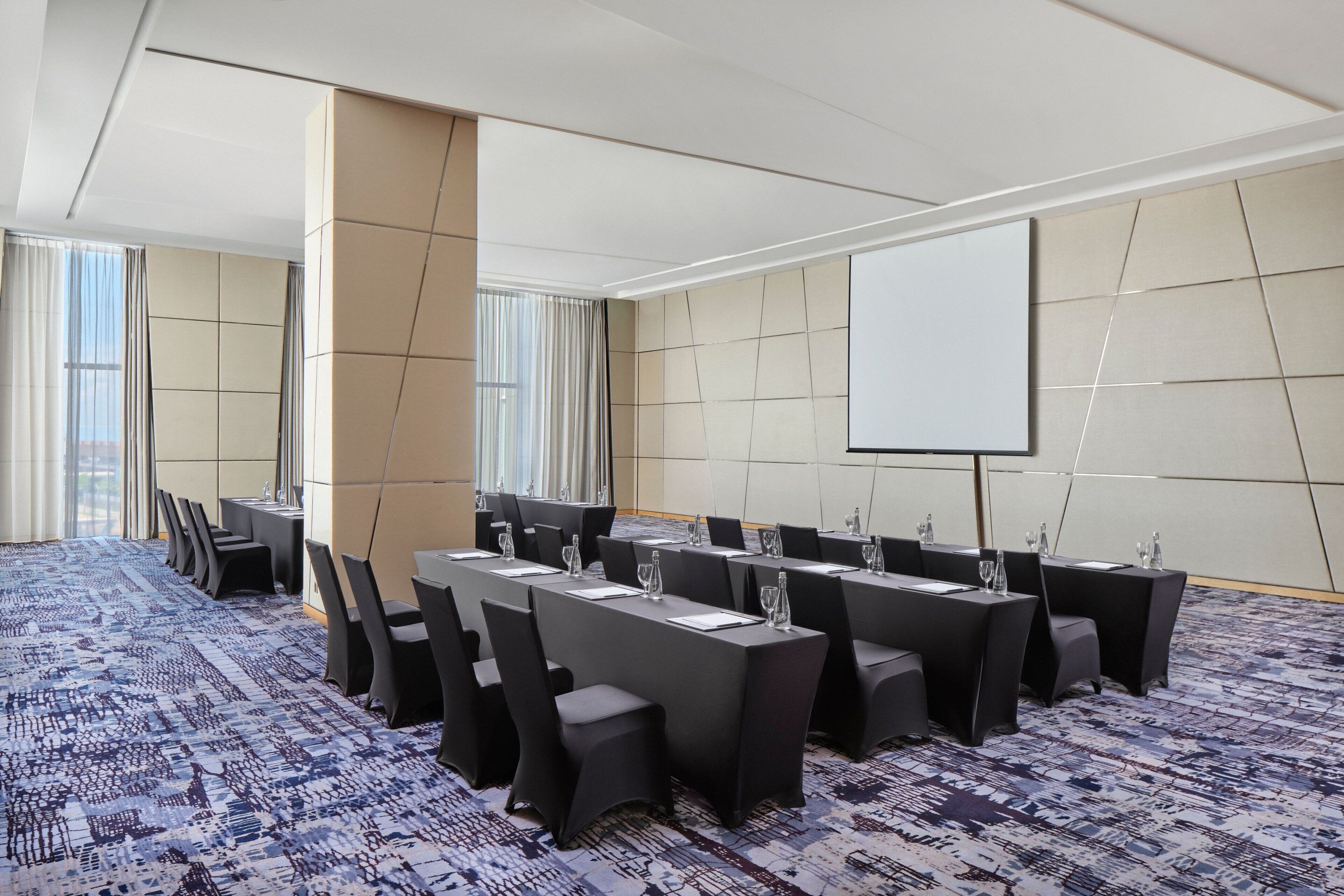 A conference room with long tables, chairs, and a projector screen.