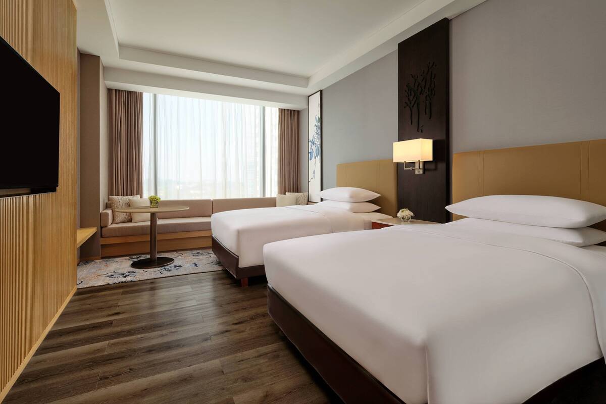 Una habitación de hotel con dos camas, televisión, una mesita y una ventana con cortinas.