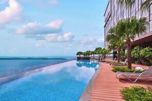 A swimming pool with a wooden deck and lounge chairs, overlooking a body of water and a distant shoreline. - Batam Marriott Hotel Harbour Bay (Batam)