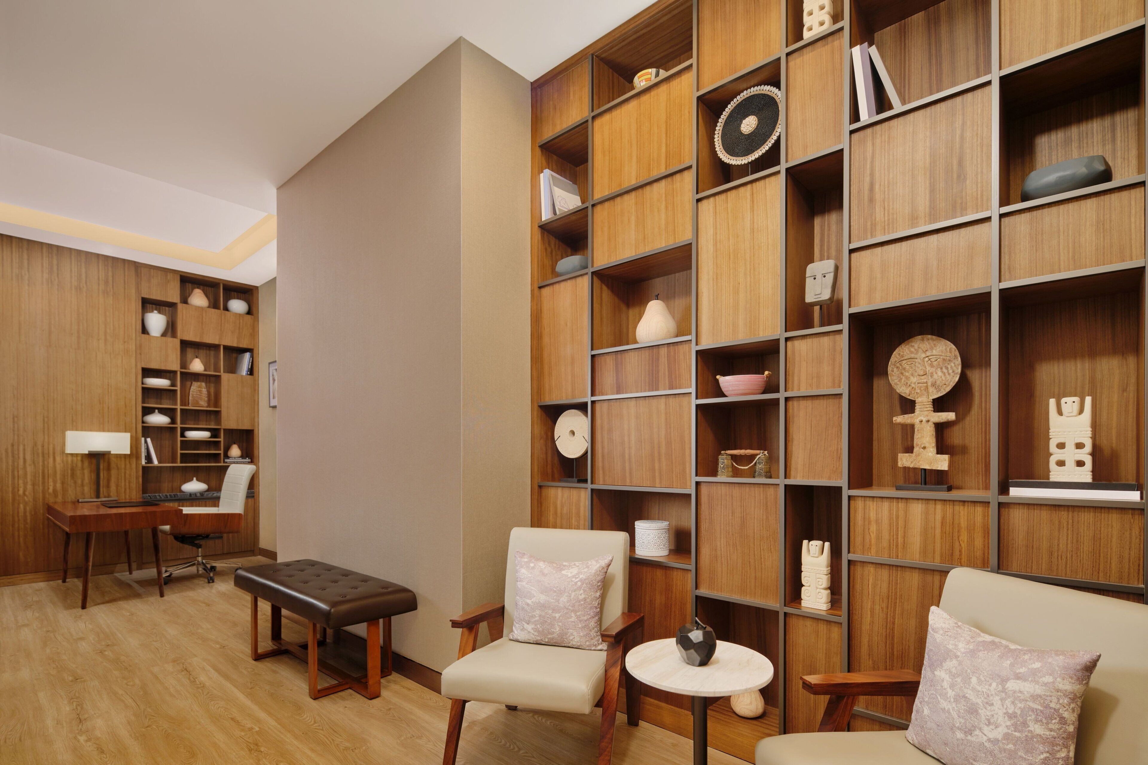 A modern room with a wooden bookshelf, a desk, two chairs, and a small round table.