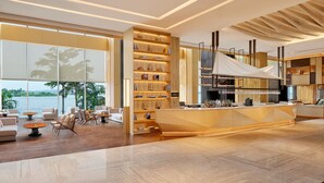 A modern hotel lobby with a wooden reception desk, seating area, and large windows overlooking a body of water.