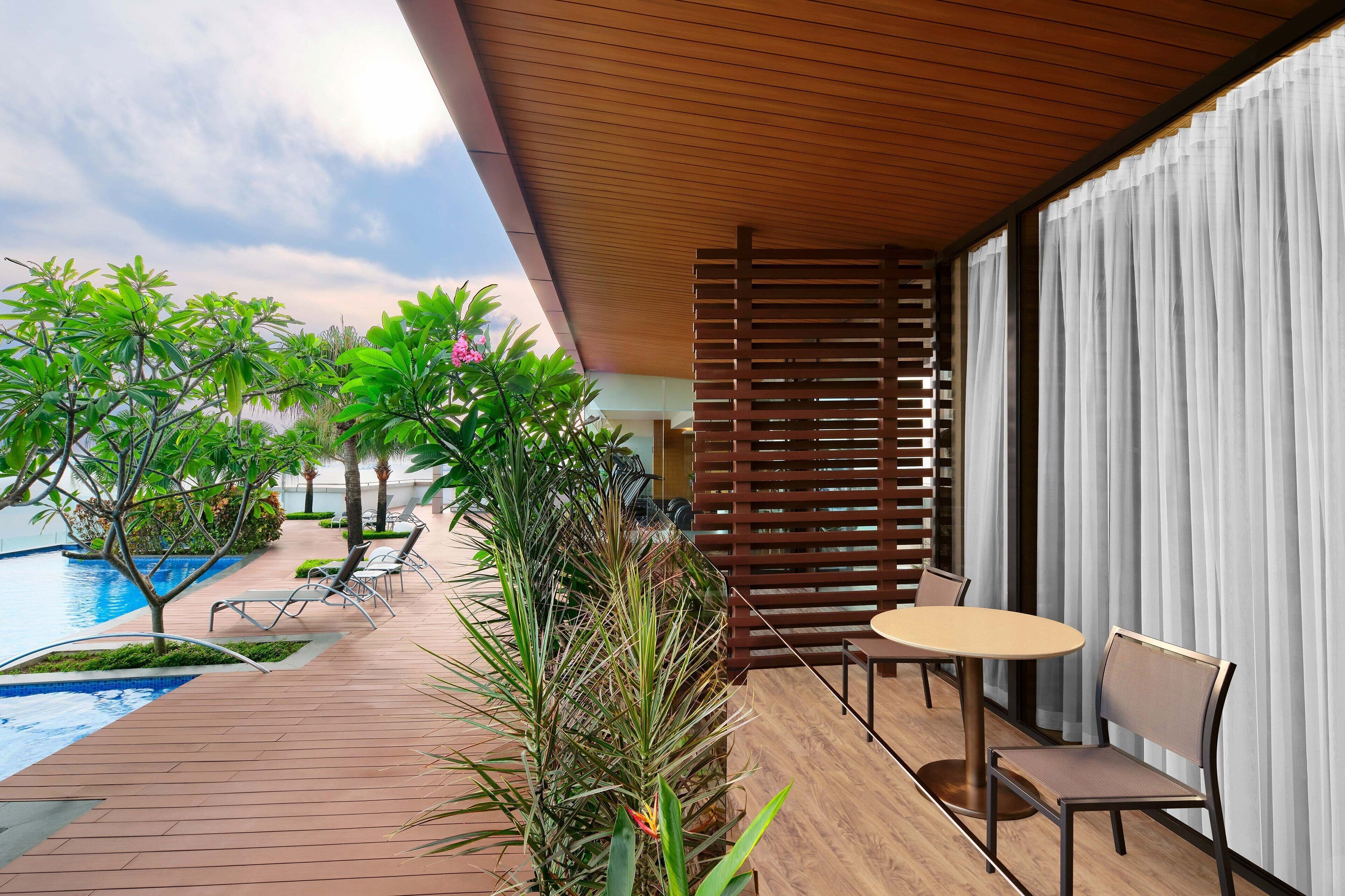 A modern outdoor seating area with a pool, wooden deck, and lush greenery.