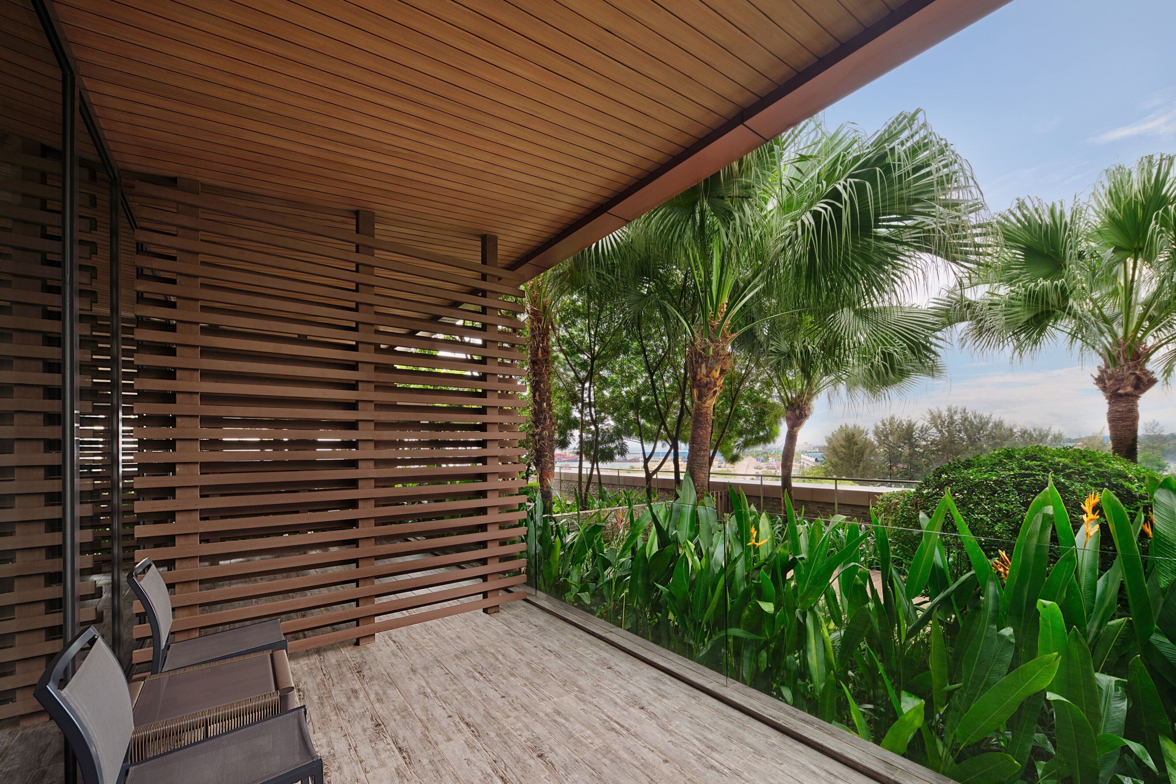 Un espace extérieur aménagé, abrité et doté de sièges, avec des lambris en bois, un banc et une végétation luxuriante comprenant des palmiers et des plantes tropicales.