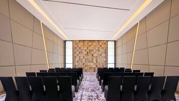 A conference room with rows of chairs, a patterned carpet, and a wooden wall panel.