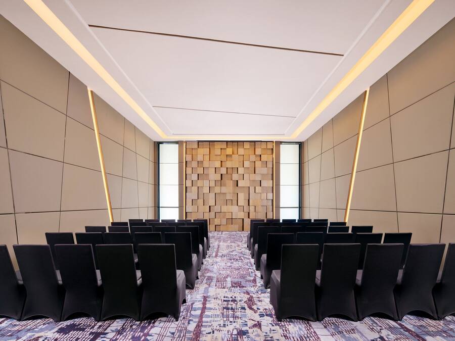 A conference room with rows of chairs, a patterned carpet, and a wooden wall panel.